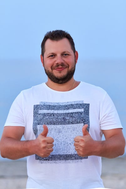 A young handsome positive guy smiles and shows OK. Portrait of a bearded guy with a pleasant appearance. The dark-haired guy on the beach.